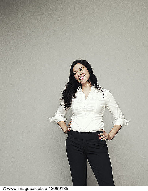 Happy woman with hands on hip standing against gray background