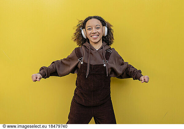 Happy woman with headphones dancing in front of yellow wall