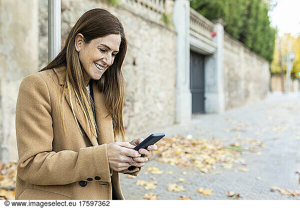 Happy woman with long brown hair text messaging through smart phone