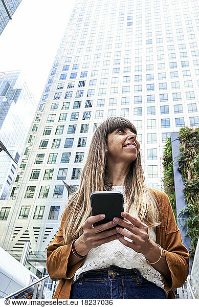 Happy woman with mobile phone in front of building