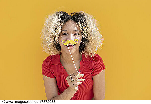 Happy woman with mustache prop in front of yellow wall