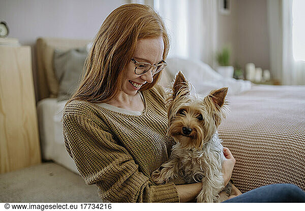 Happy woman with pet dog sitting by bed at home