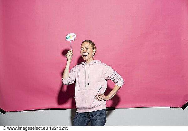 Happy woman with prop and hand on hip over pink background