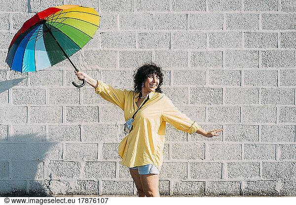 Happy woman with rainbow umbrella posing in front of wall