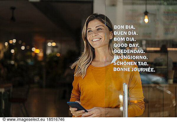 Happy woman with smart phone standing by door at cafe