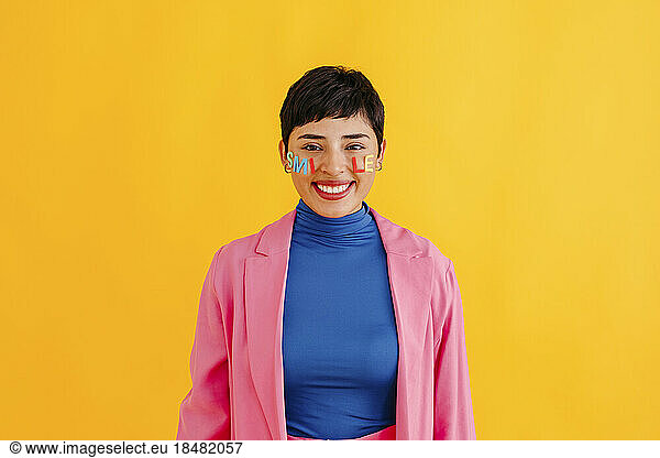 Happy woman with smile text sticker on cheeks standing against colored background