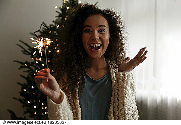 Happy woman with sparkler standing in front of Christmas tree