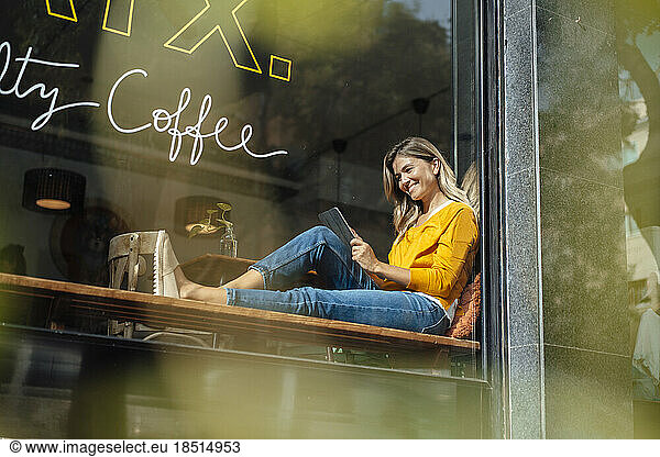 Happy woman with tablet PC sitting by window in cafe