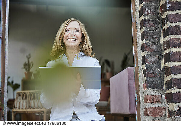 Happy woman with tablet PC sitting on doorway