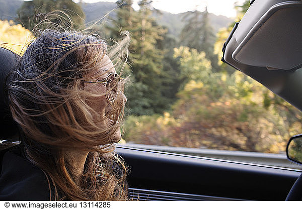Happy woman with tousled hair riding in convertible car