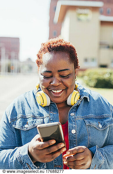 Happy woman with wireless headphones using smart phone in the street