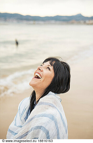 Happy woman wrapped in scarf laughing at beach