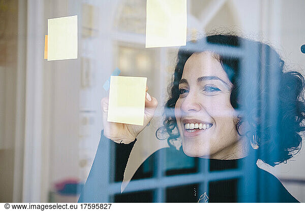 Happy woman writing on adhesive note on window