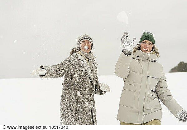 Happy women enjoying throwing snowball in winter