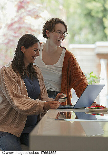 Happy women friends online shopping at laptop in kitchen