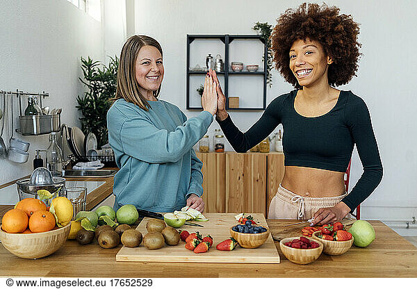 Happy women giving high-five to each other standing at table in kitchen