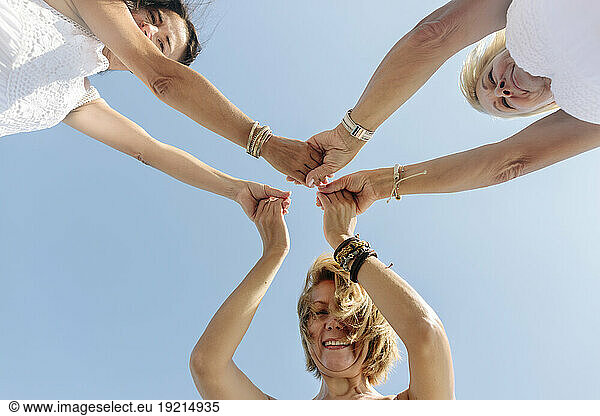 Happy women holding hands under sky