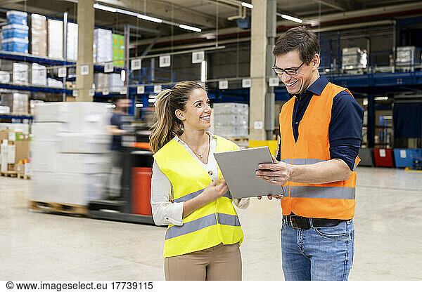 Happy worker discussing over tablet PC with young colleague in warehouse