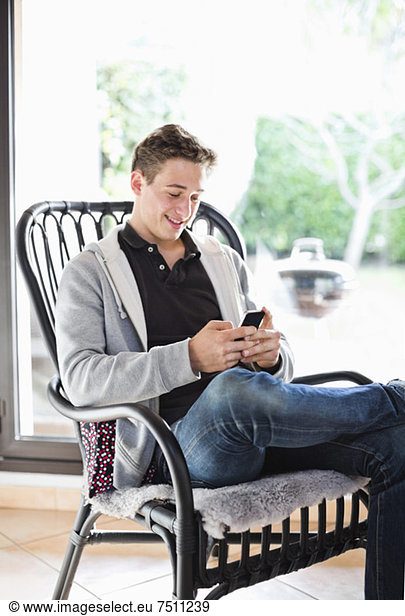 Happy young boy text messaging while relaxing on armchair at home