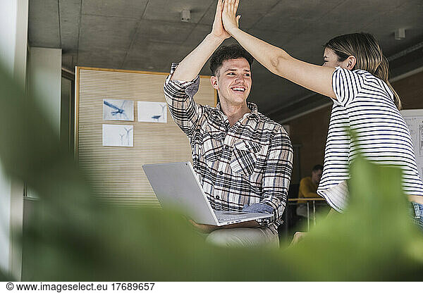 Happy young businessman and businesswoman high fiving in office