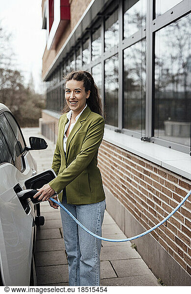 Happy young businesswoman charging electric car