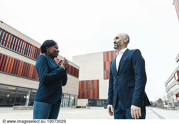 Happy young businesswoman having discussion with businessman in office park