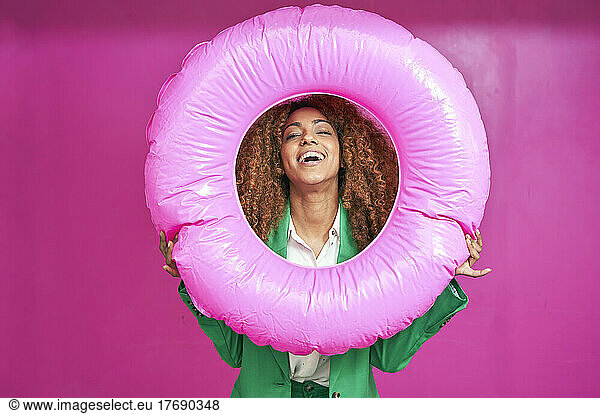 Happy young businesswoman looking though inflatable ring against pink background