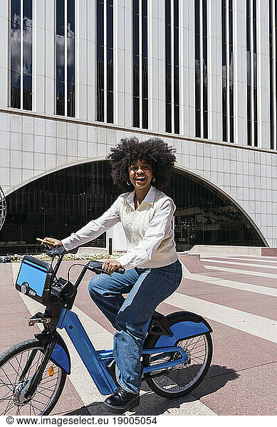 Happy young businesswoman riding bicycle in office park on sunny day