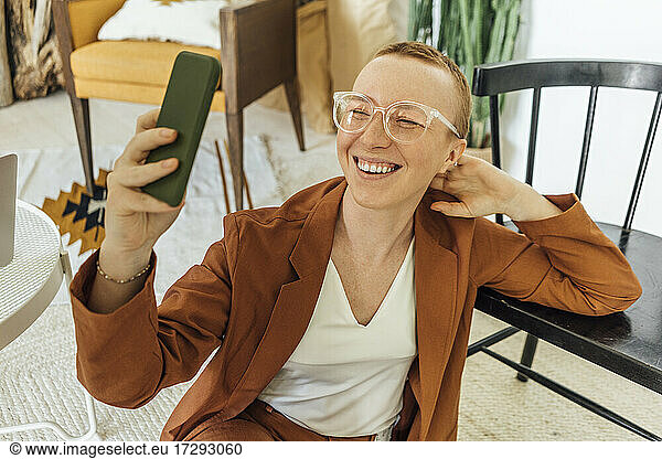Happy young businesswoman taking selfie through smart phone at work place