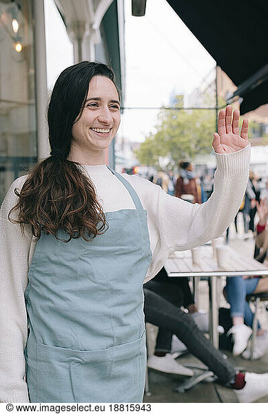 Happy young cafe owner waving hand
