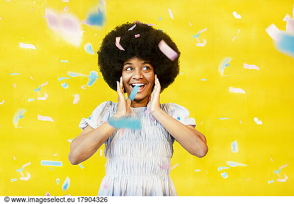 Happy young celebrating with confetti against yellow background