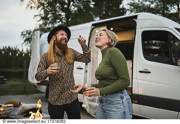 Happy young couple dancing by camping van in evening