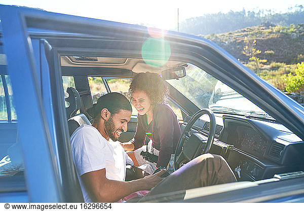 Happy young couple laughing on road trip in sunny car