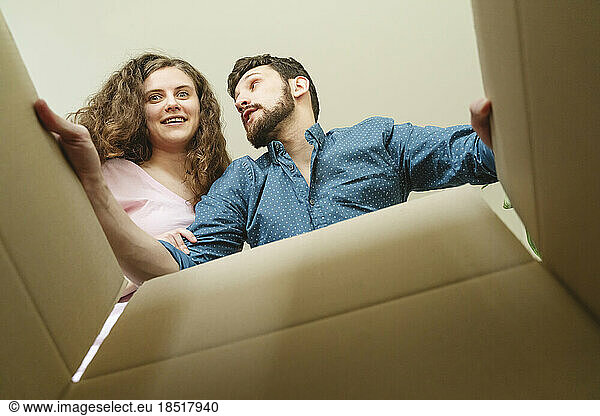 Happy young couple opening cardboard box in new home