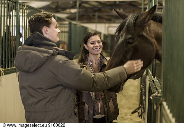 Happy young couple stroking horse in stable
