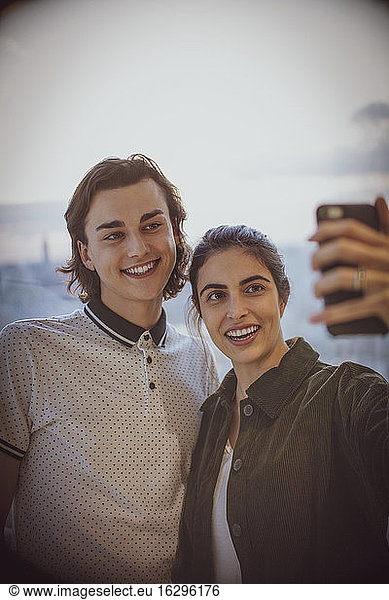Happy young couple taking selfie with camera phone at window