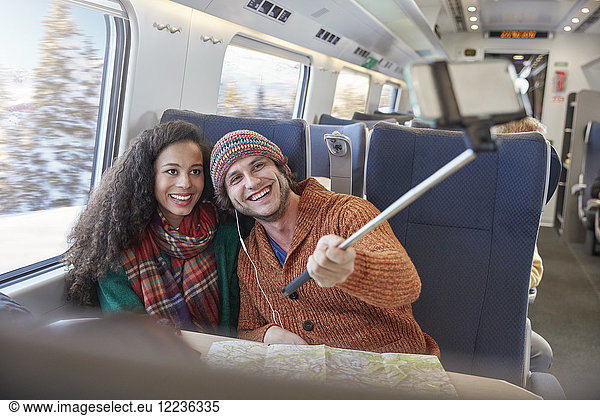 Happy young couple taking selfie with selfie stick on passenger train
