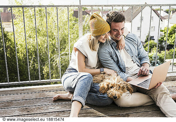 Happy young couple using laptop together on balcony