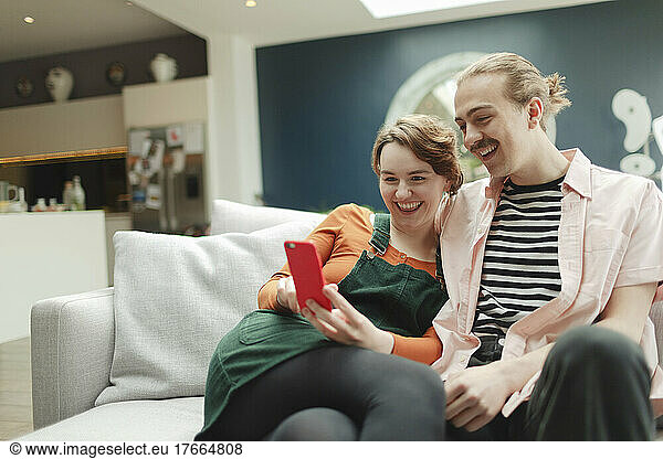 Happy young couple with smart phone on living room sofa