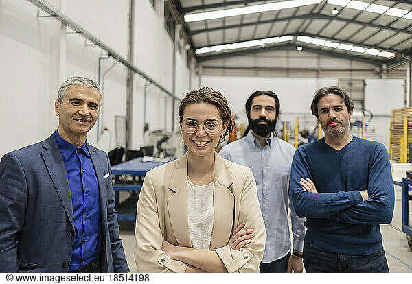 Happy young engineer standing with colleagues at factory