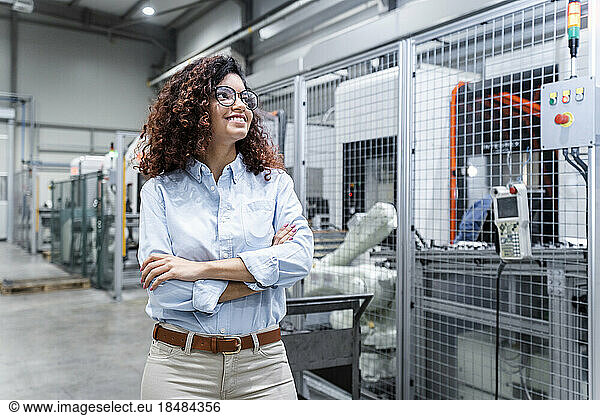 Happy young engineer with arms crossed standing in factory