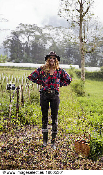 Happy young farmer standing with hands on hip in field