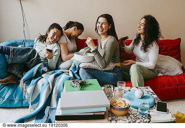 Happy young female friends sitting on sofa at home