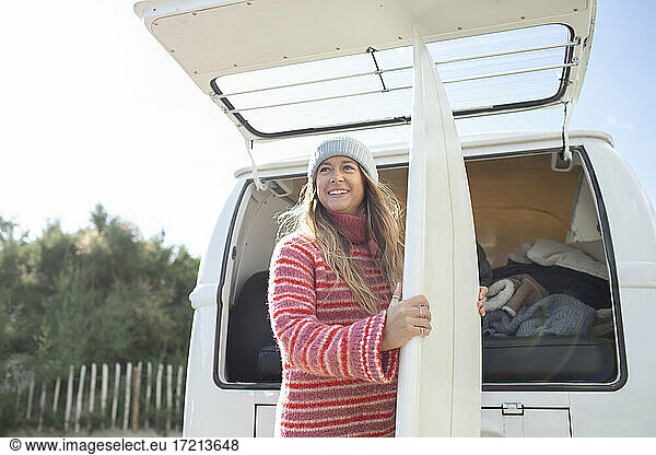 Happy young female surfer with surfboard at back of camper van