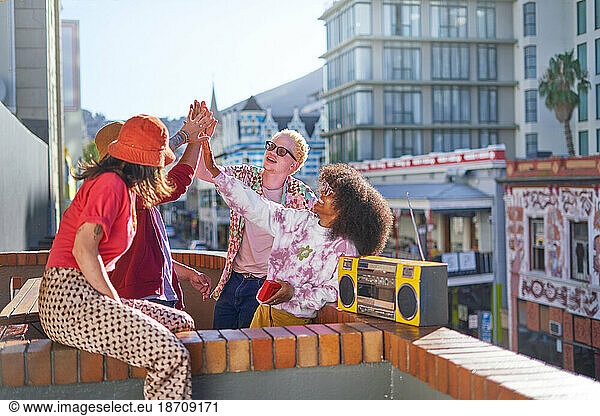 Happy young friends high-fiving on sunny urban city balcony