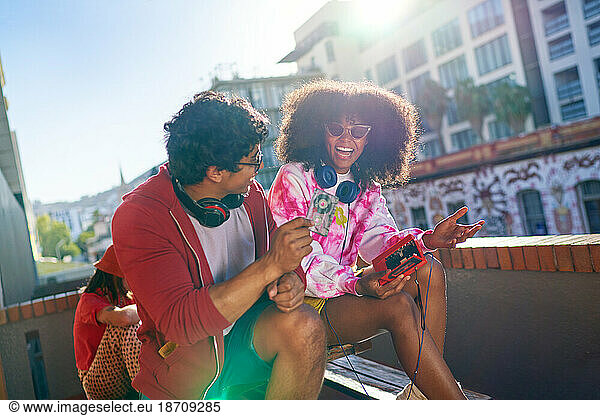 Happy young friends listening to music on sunny urban balcony