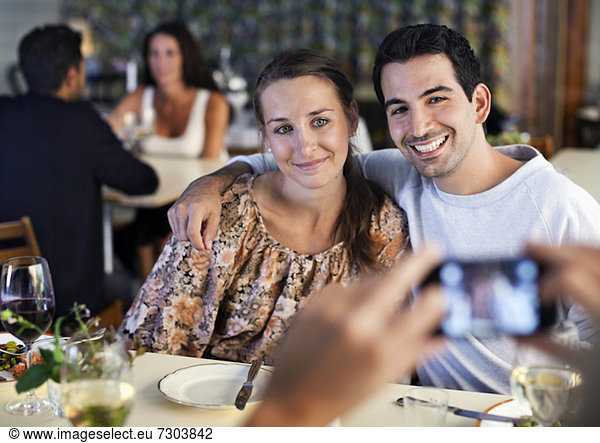 Happy young friends posing for photograph at restaurant table with people in the background