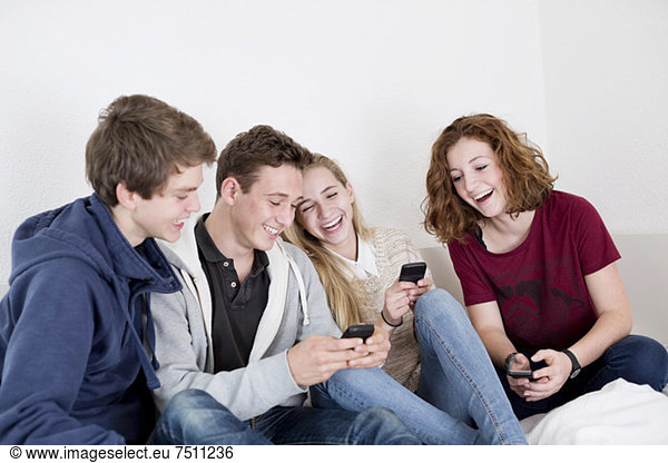 Happy young friends using mobile phones at home