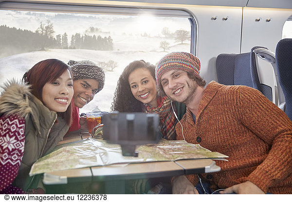 Happy young friends with map taking selfie with selfie stick on passenger train