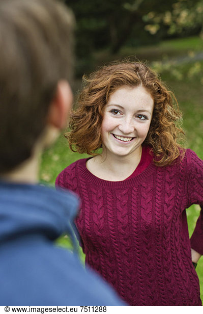 Happy young girl looking at male friend while standing at park
